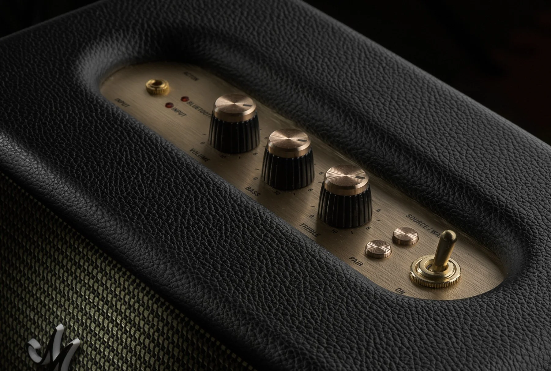 Close-up of a guitar amplifier control panel with black textured surface, gold knobs, and brushed metal faceplate.