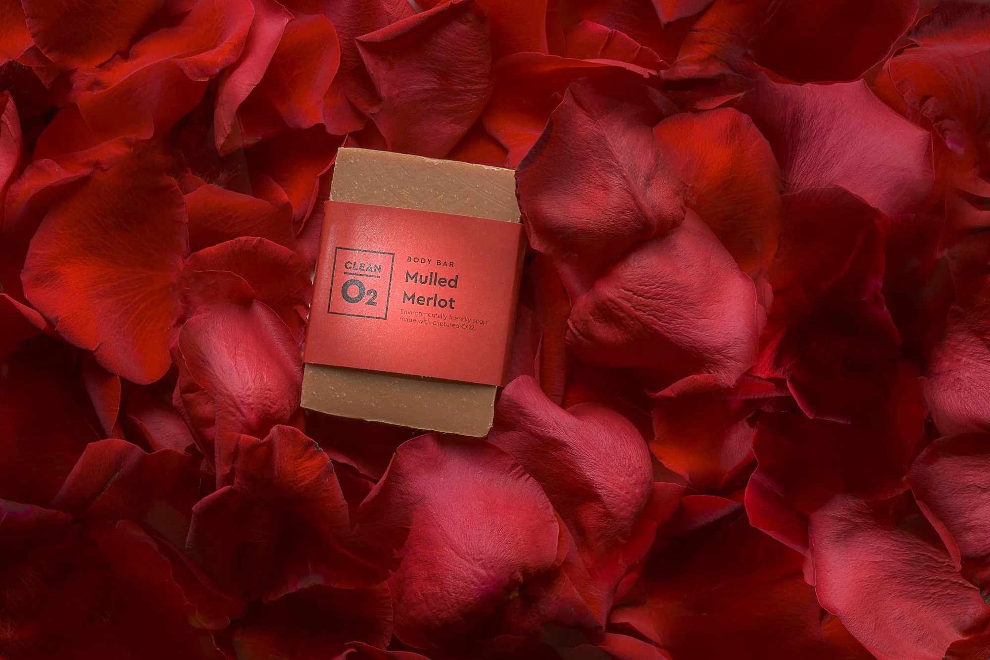 A bar of mulled merlot scented soap labeled 'Clean O2' resting on a bed of red rose petals.