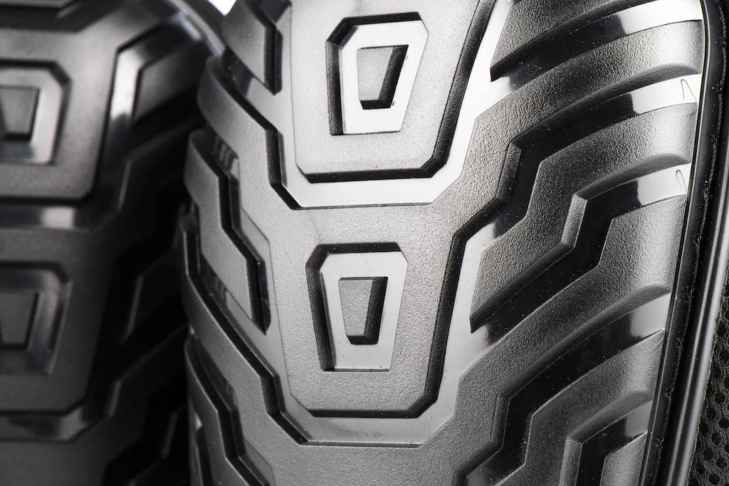 Close-up of a black rubber tire tread with angular patterns and deep grooves.