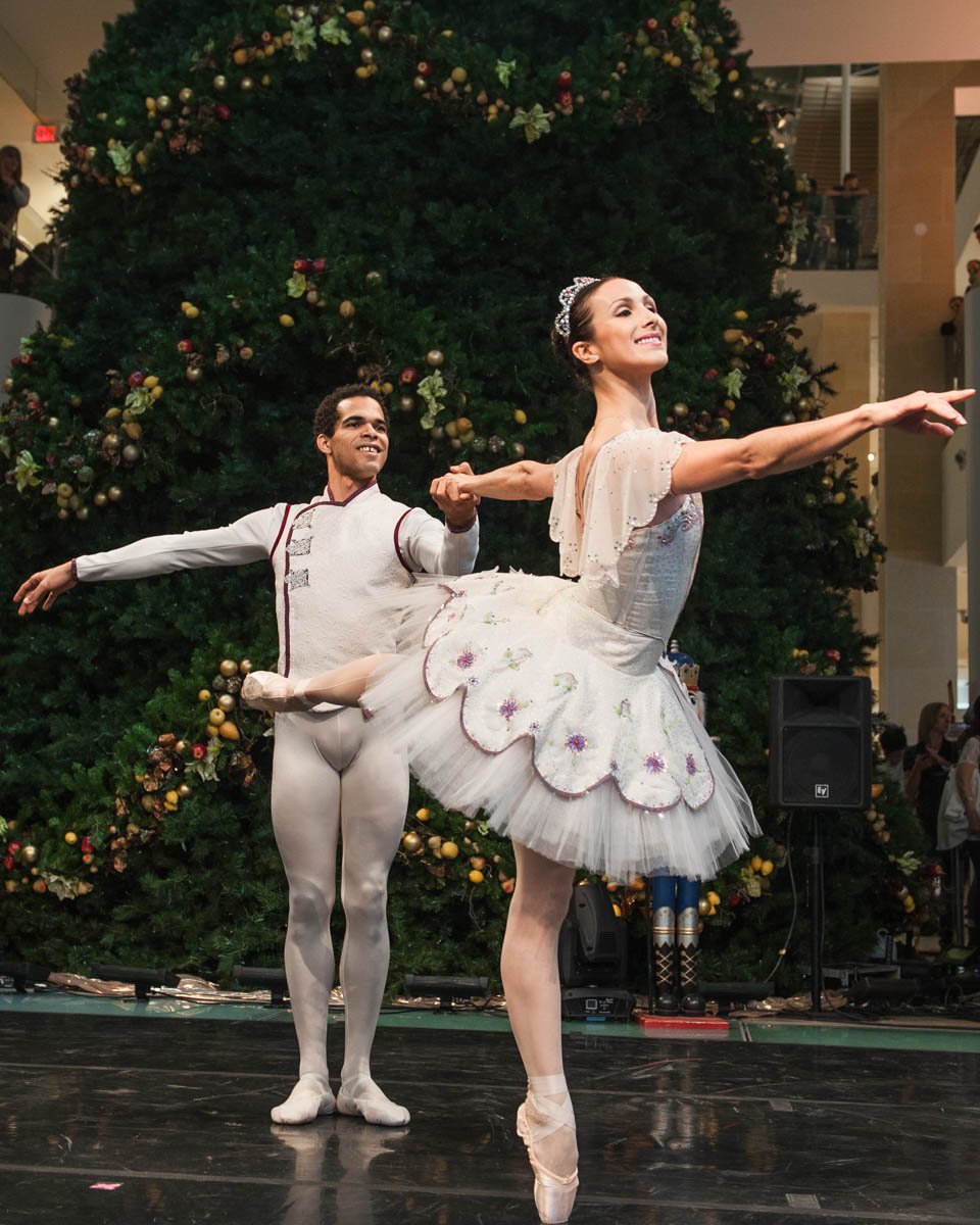 Ballet dancers performing on stage in front of a decorated Christmas tree.