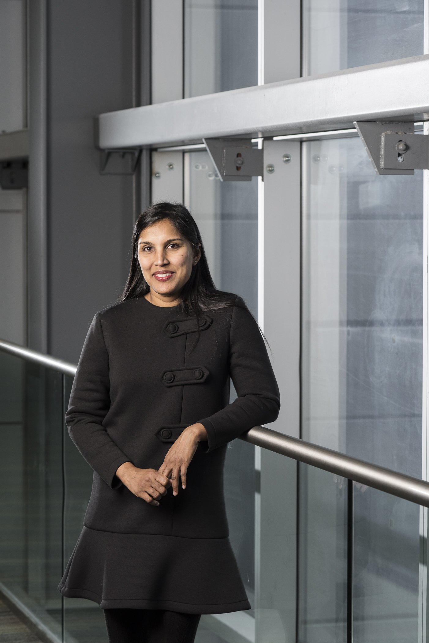 A woman in a black coat standing by a glass railing in a modern building