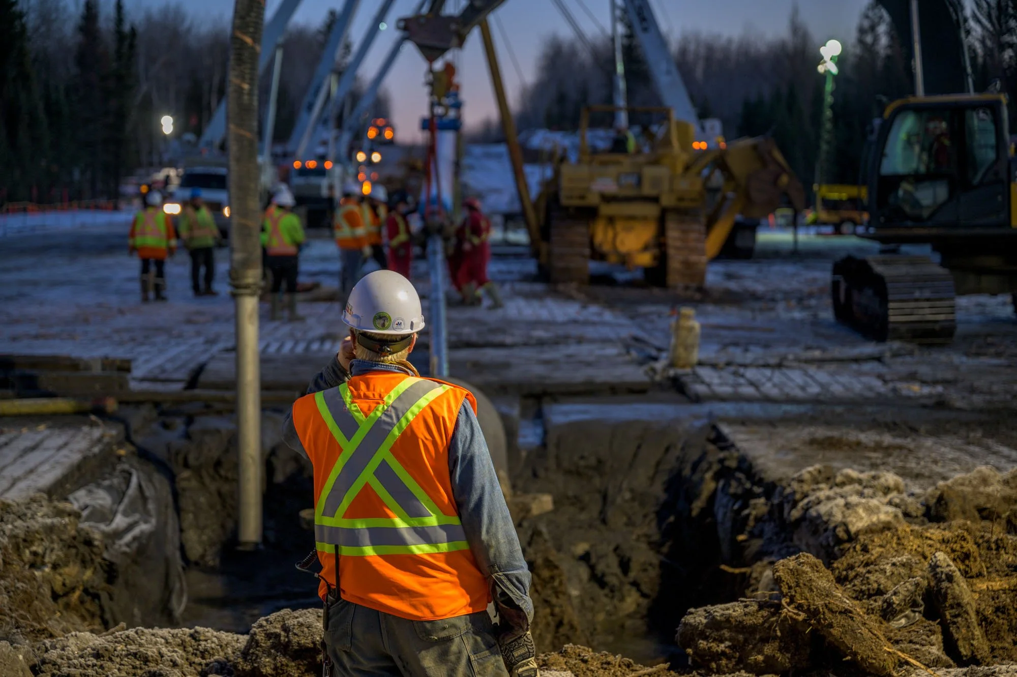 Construction workers at a railroad construction site during dusk, with machinery and workers in safety gear.