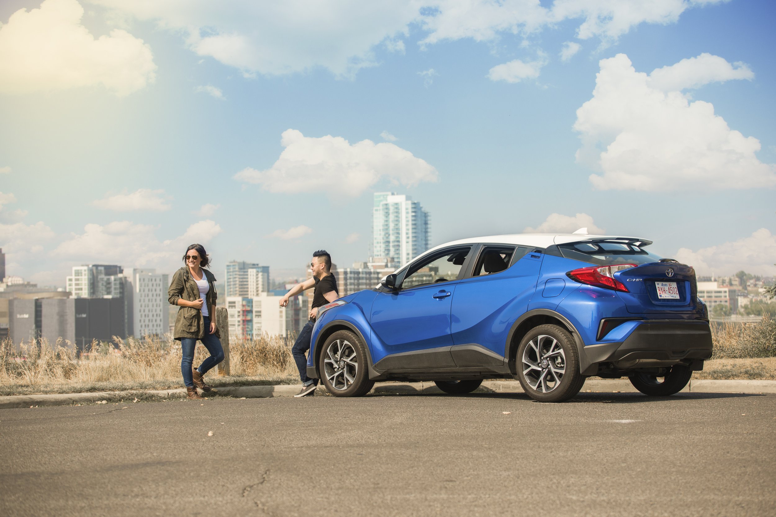 Two women and one man standing next to a blue Toyota C-HR on a city street with a skyline in the background.