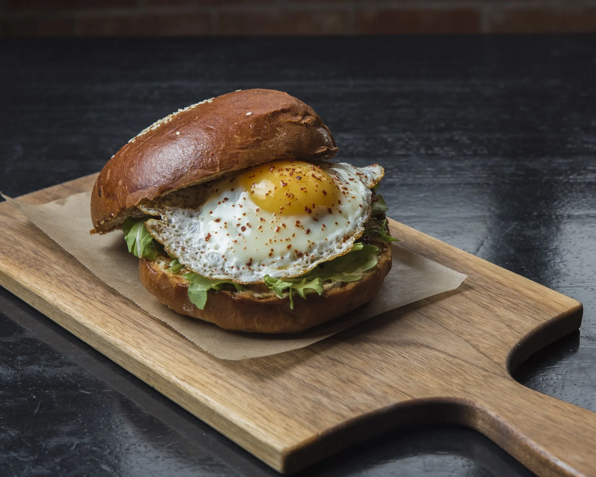 A sandwich with a fried egg, lettuce, and a bun on a wooden serving board.