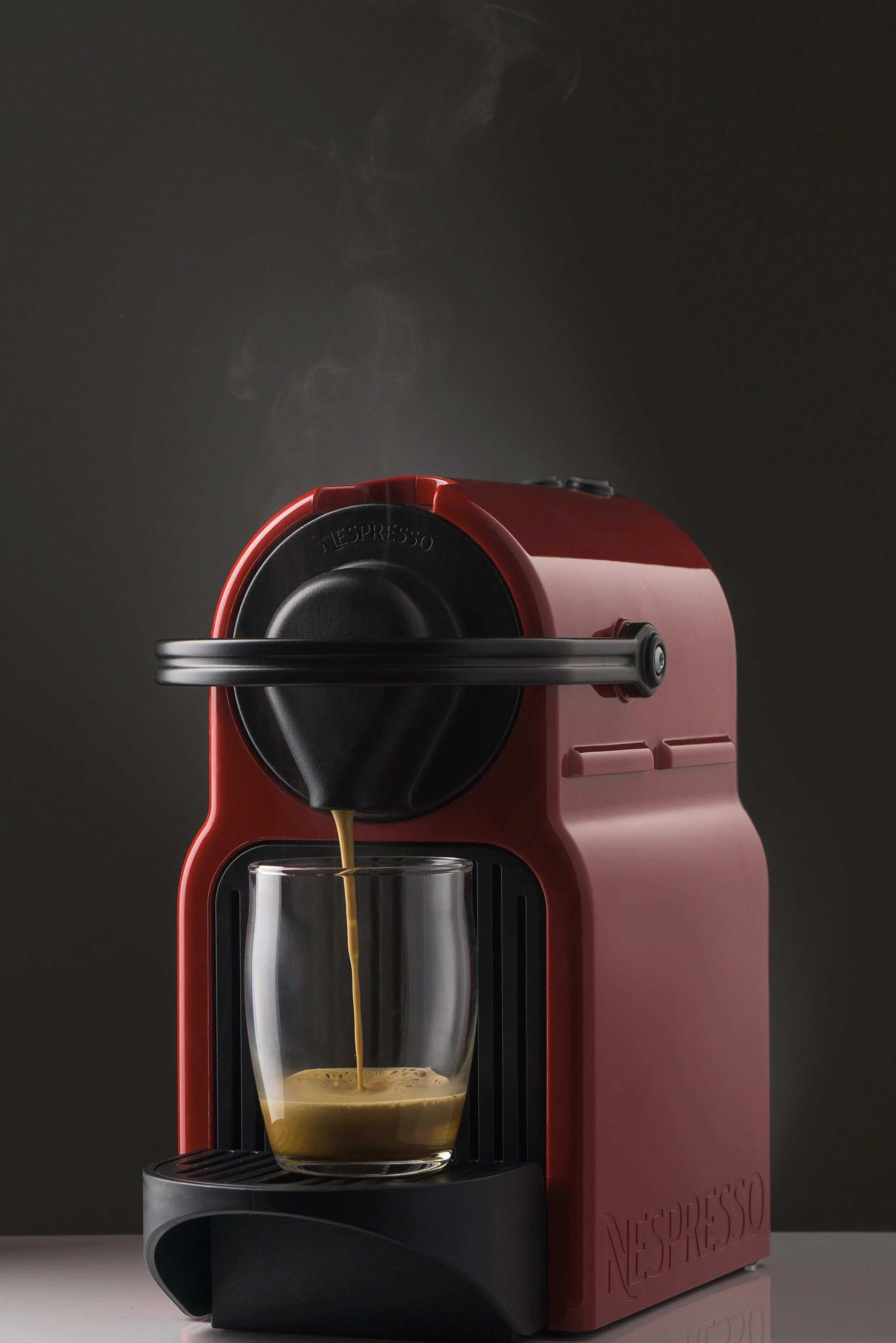 Red Nespresso coffee machine dispensing hot coffee into a glass cup with steam rising.