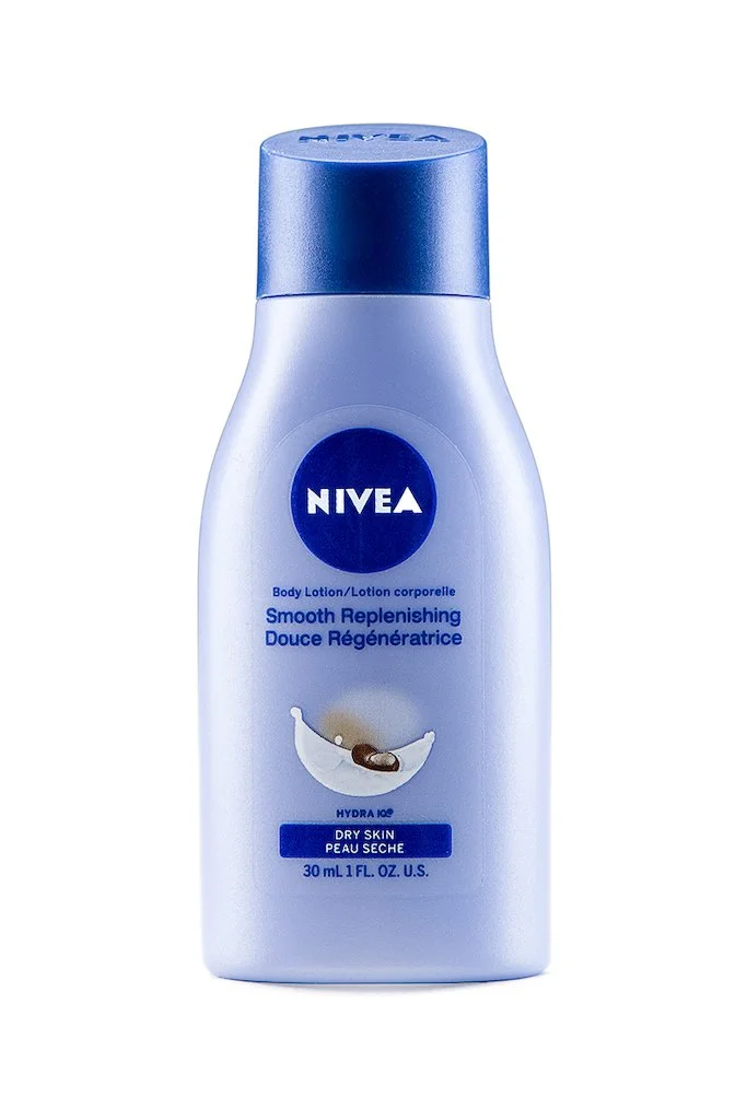 A Nivea body lotion bottle labeled 'Smooth Replenishing' for dry skin, 30 ml, with a blue cap and white body, featuring a graphic of a crescent moon with a capsule and water droplets.