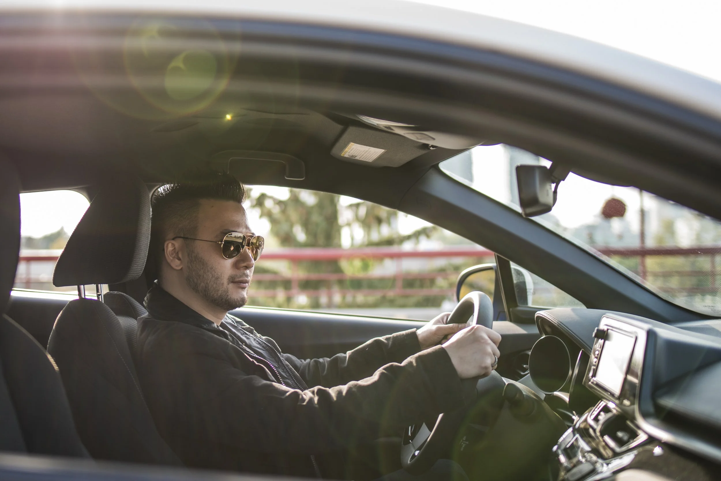 Man wearing sunglasses driving a car, seen from inside the vehicle.