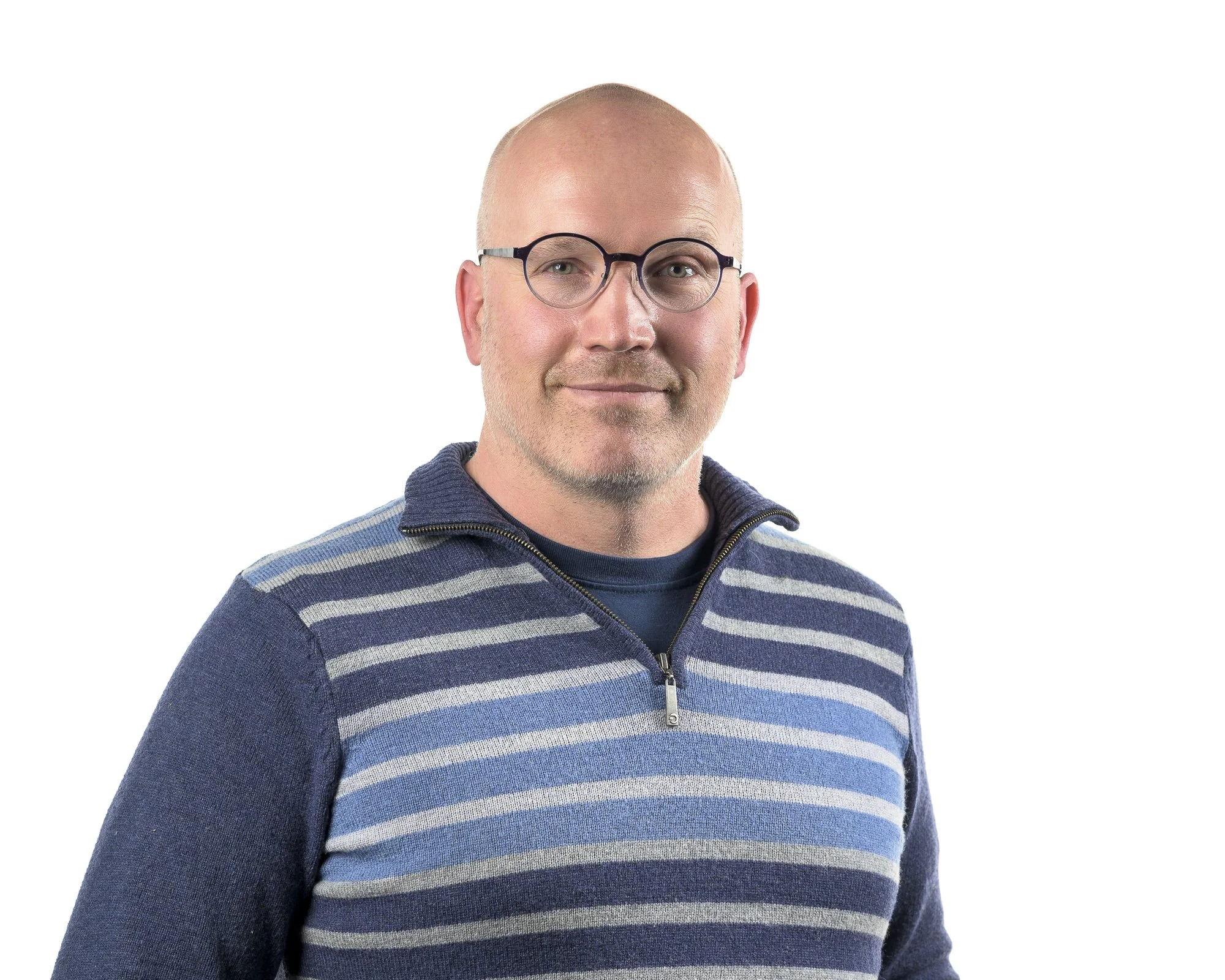 A bald man with glasses and a light beard wearing a blue and gray striped sweater, smiling against a white background.