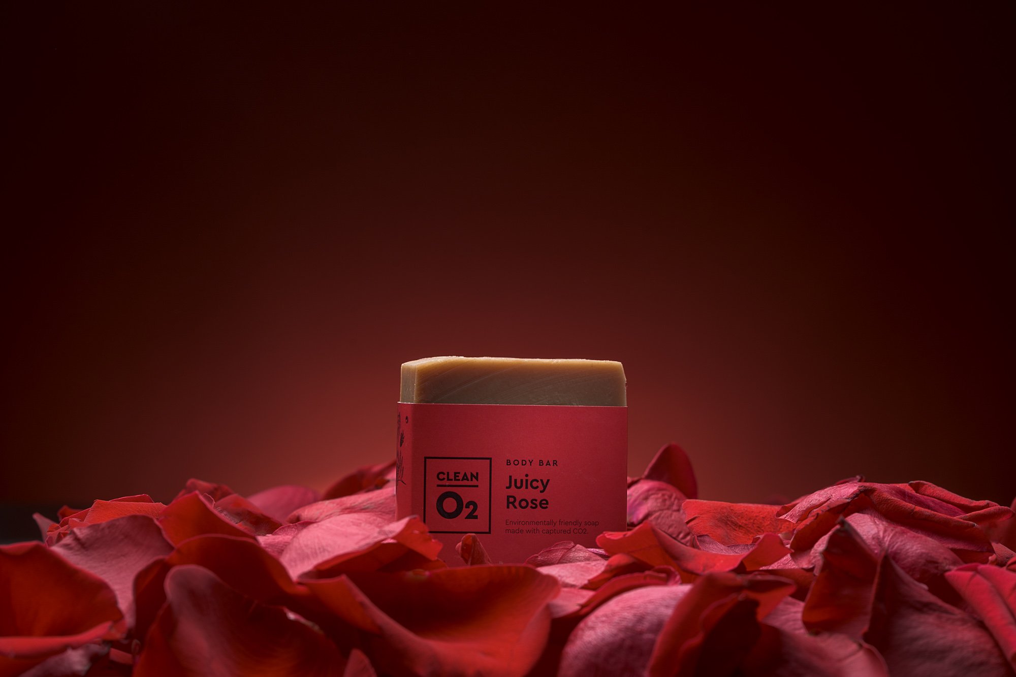 A bar of soap labeled 'Juicy Rose' on a bed of pink rose petals with a dark red background.
