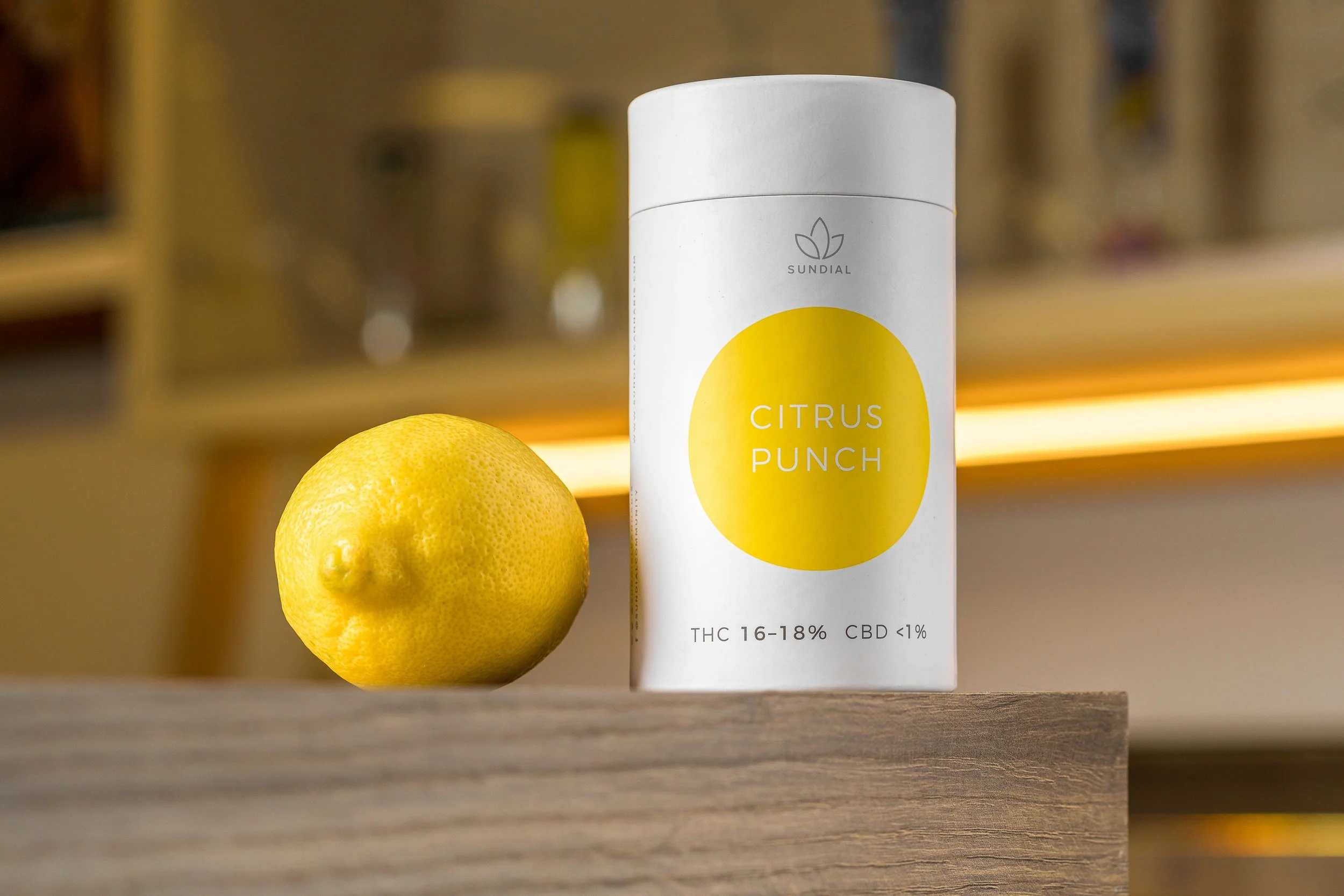 A lemon and a white container labeled 'Citrus Punch' with a yellow circle on it, on a wooden surface.