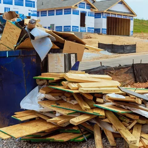 Construction site with a large pile of wood, cardboard, and debris in front of a partially built house with blue insulation panels.