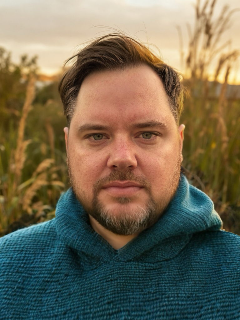 Close-up of a Nick Richtsmeier, wearing a teal hoodie, outdoors during sunset with tall grass in the background.