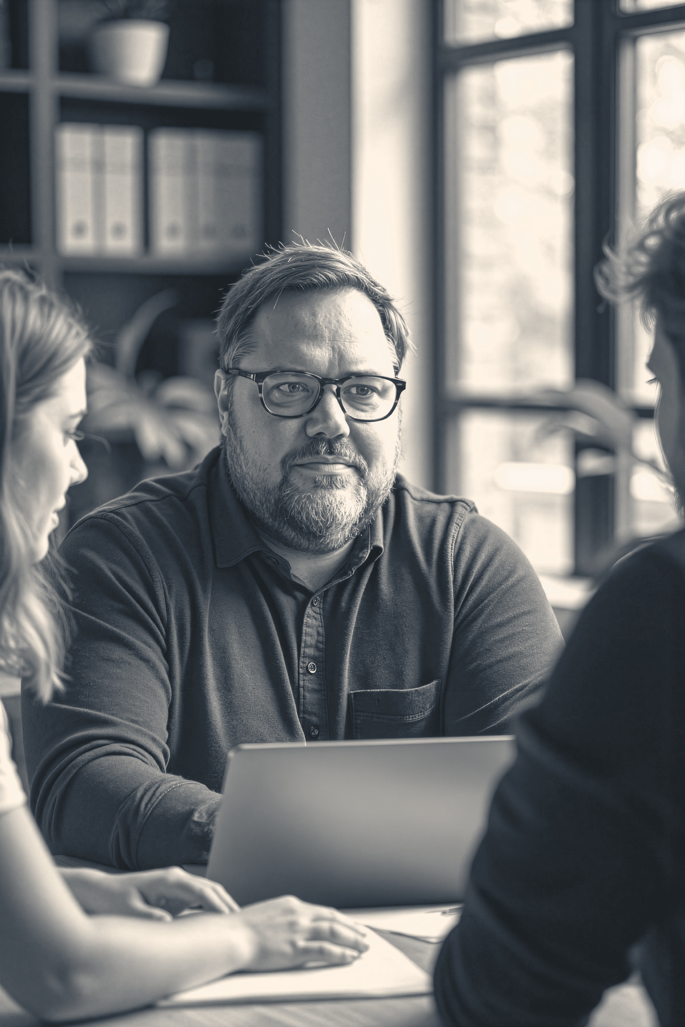 Group of people having a discussion in a meeting, with a man wearing glasses at the center.
