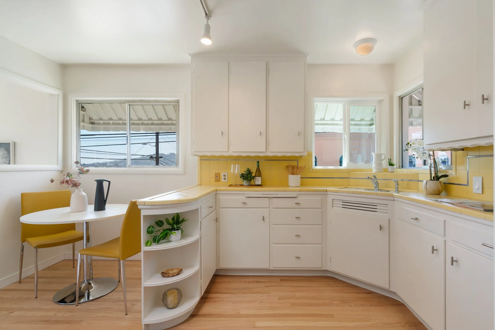 A bright kitchen with white cabinets, yellow tiled backsplash, and a small dining area with yellow chairs and a white round table.