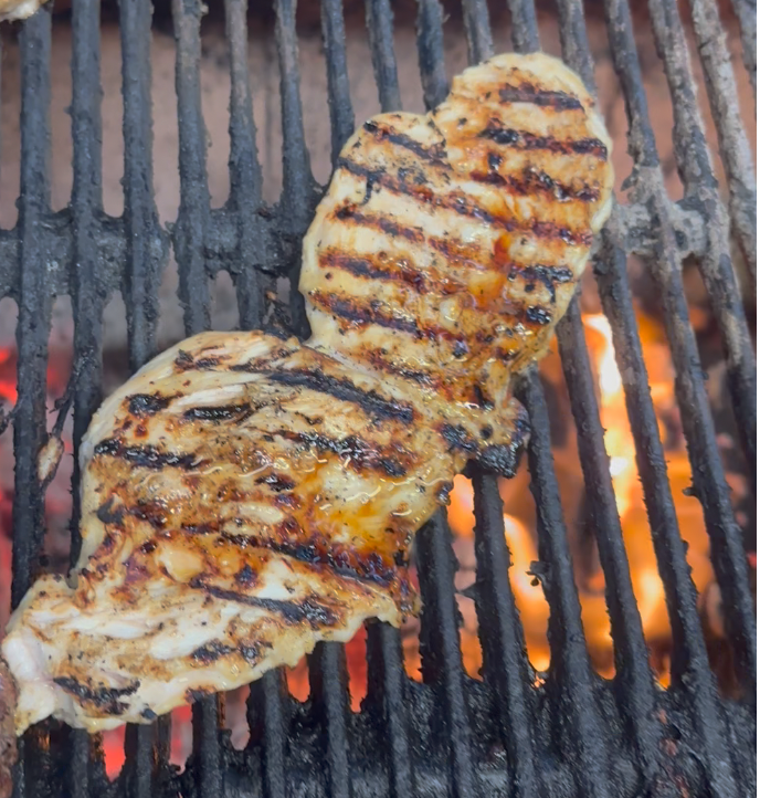 Grilled chicken breast with grill marks cooking on a barbecue grill over open flame.