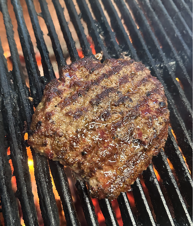 A juicy, grilled beef patty cooking on a barbecue grill.