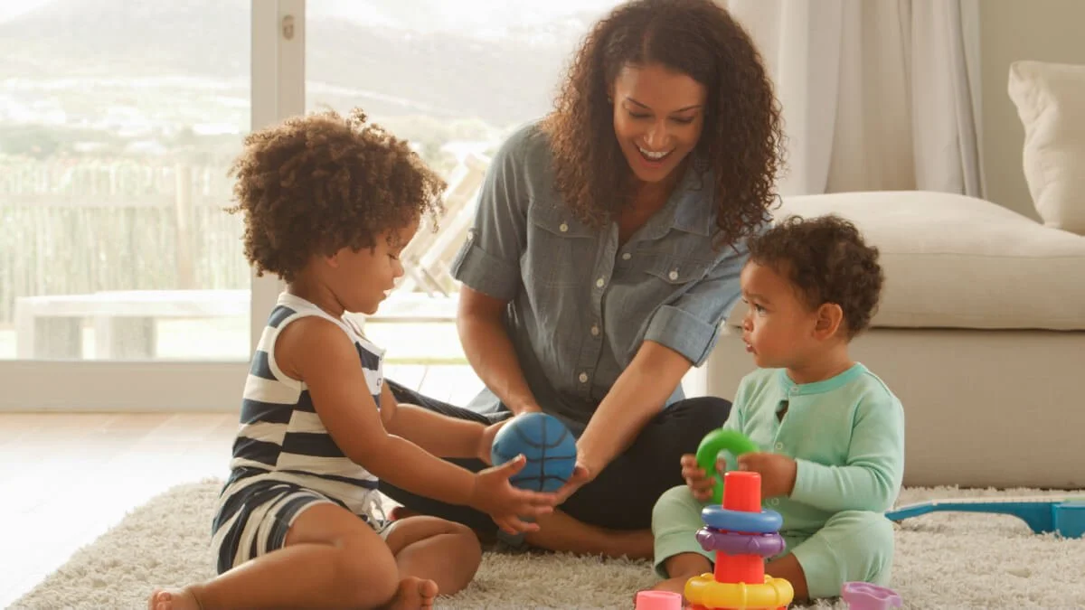 Mother playing on the floor with two young children using toys to support language development and early learning through play