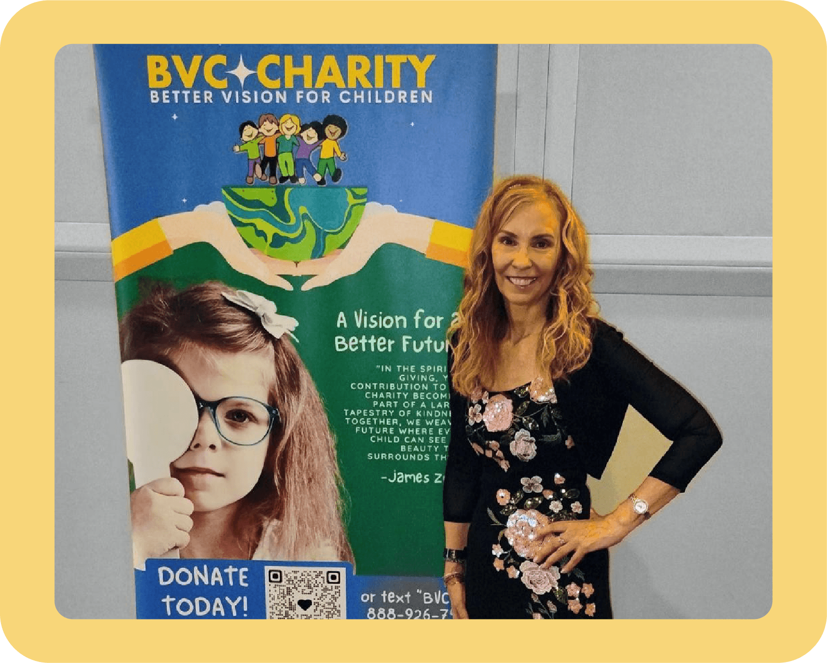A woman with curly blonde hair smiling and standing with her hand on her hip next to a large banner for BVC Charity promoting better vision for children. The banner features an image of a young girl with glasses and a quote about the charity's mission.