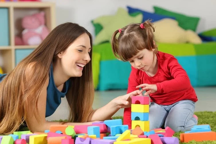 Mother and young daughter playing together on the floor, building a tower with colorful blocks