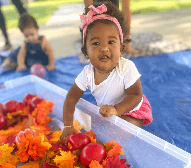 A young child exploring a fall sensory bin with leaves and toy apples, showing how repetition and play support early childhood learning.