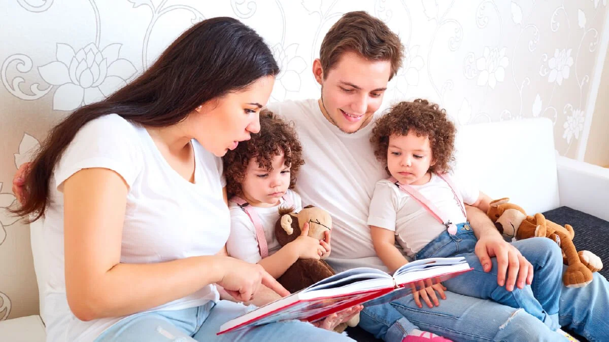 Parents reading a book with two young children on a couch while supporting early language development and communication