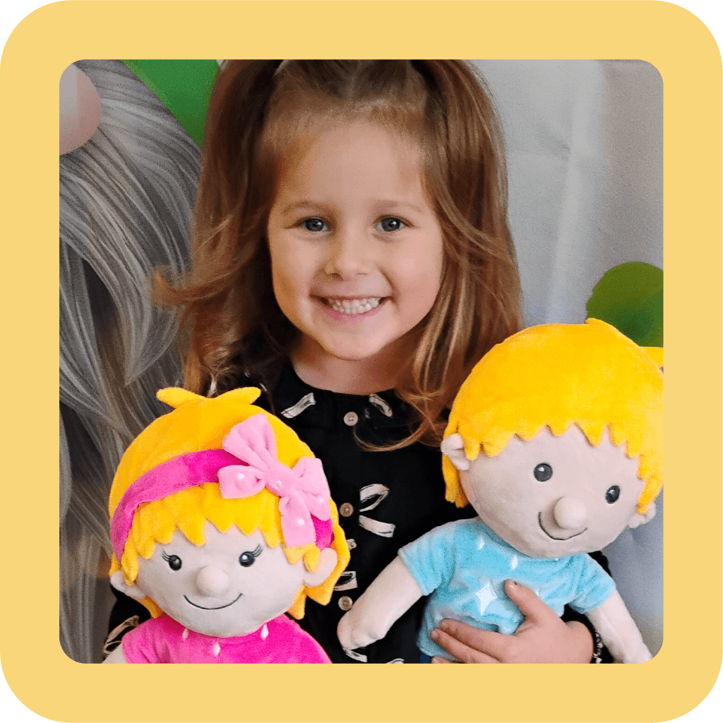 A young girl with brown hair and a big smile holding two plush dolls of children with yellow hair, Ruby and Louie, one girl with a pink dress and headband, and one boy with a blue shirt, in a room with a colorful background.