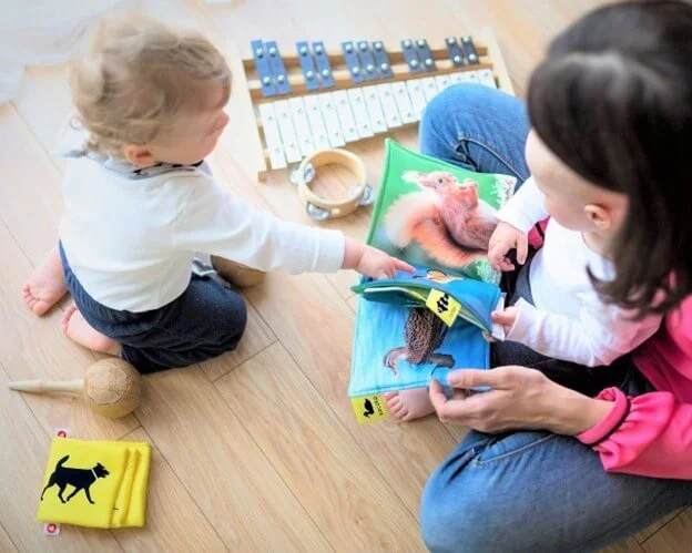 Child and parent reading a picture book together on the floor with toys and instruments during play-based language learning