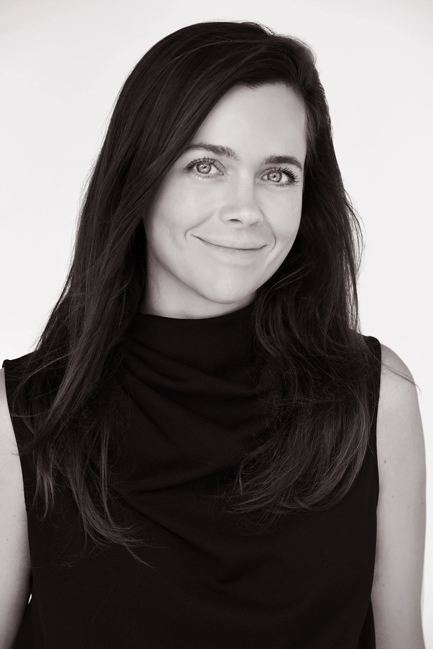Black and white portrait of a woman with long dark hair, smiling, wearing a sleeveless black top.