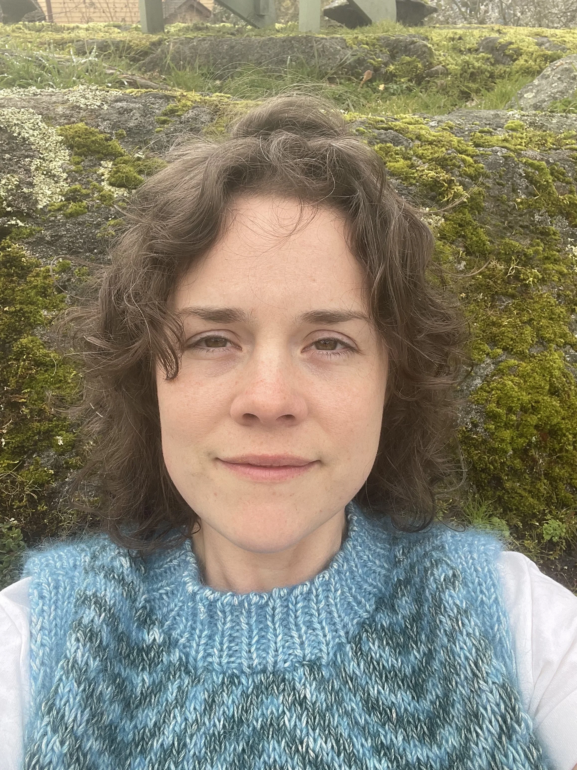 Portrait of Monika, sitting in front of a mossy rock.