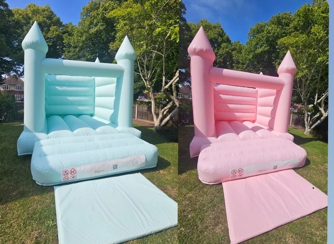 A blue bouncy castle bounce house on the left and a pink bouncy castle bounce house on the right, both set up outdoors on grass with trees in the background.