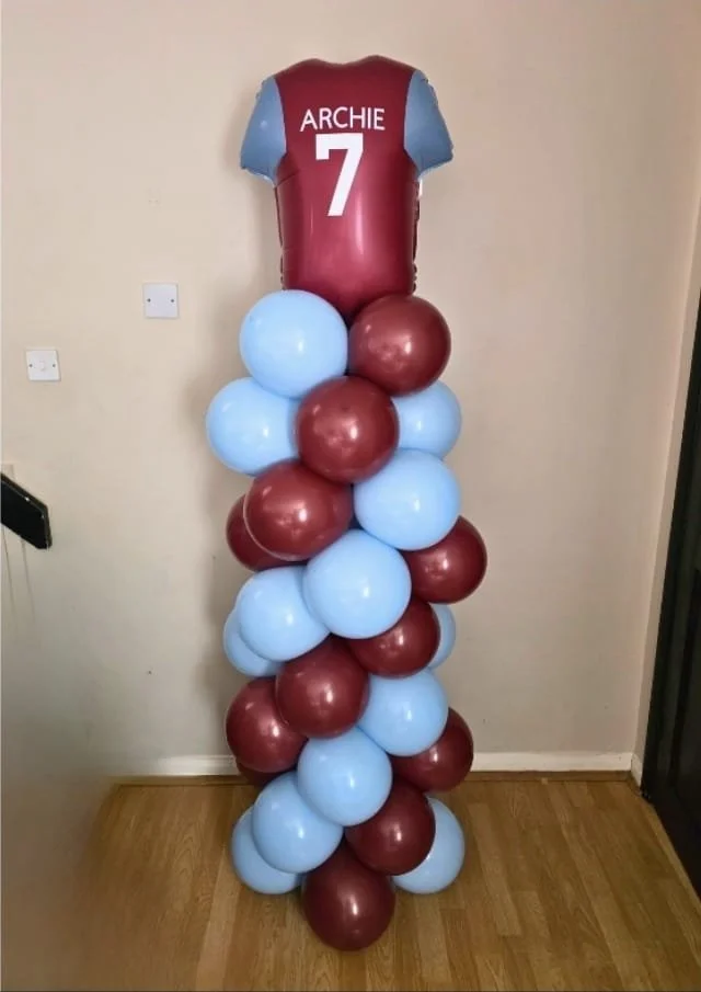 Balloon stack resembling a football jersey with the name 'Archie' and the number 7 on top, surrounded by alternating maroon and light blue balloons.