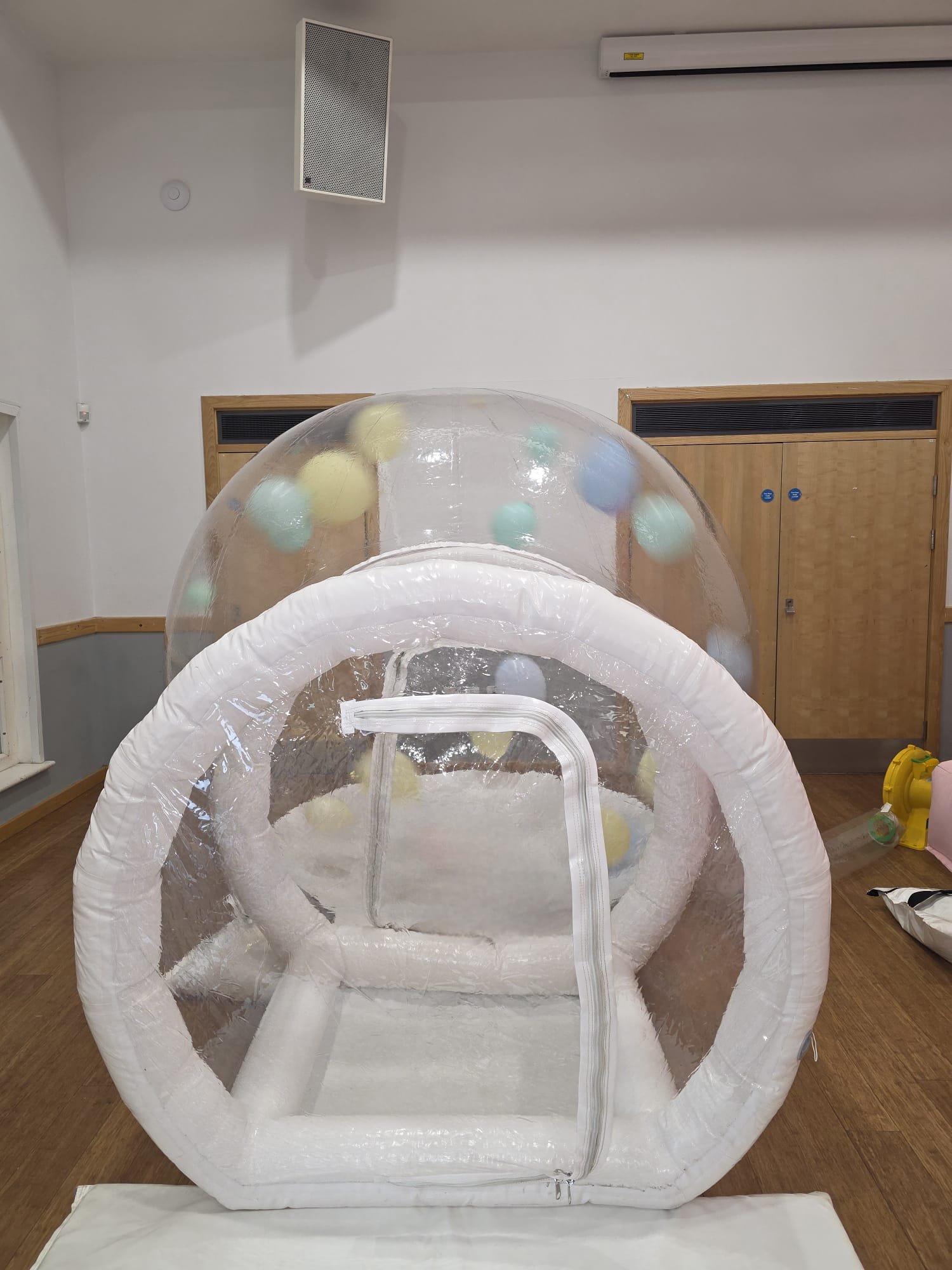 A clear inflatable bubble house with multicolored balls inside.