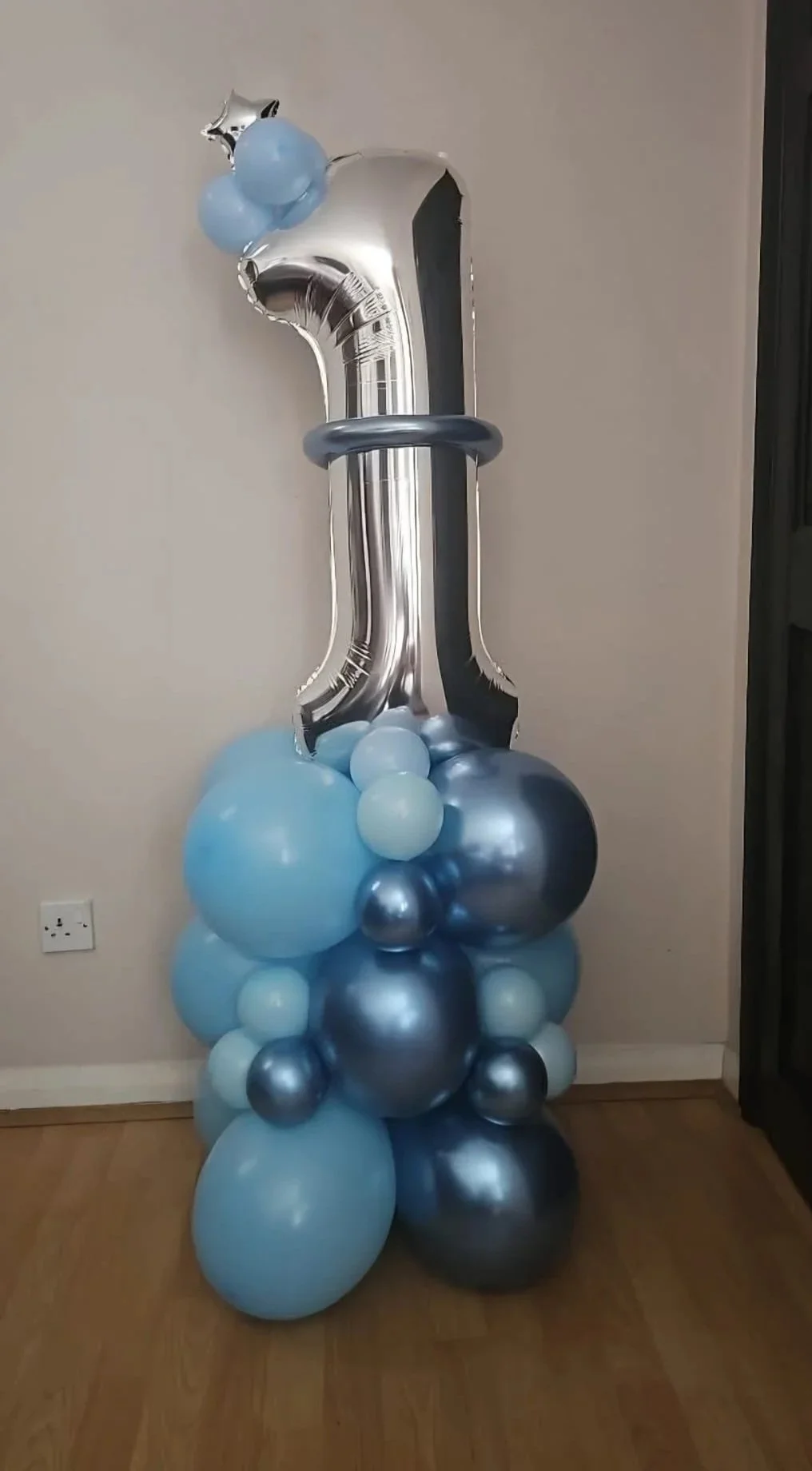 A large silver number one helium balloon with a blue and silver balloon base, decorated for a first birthday celebration.