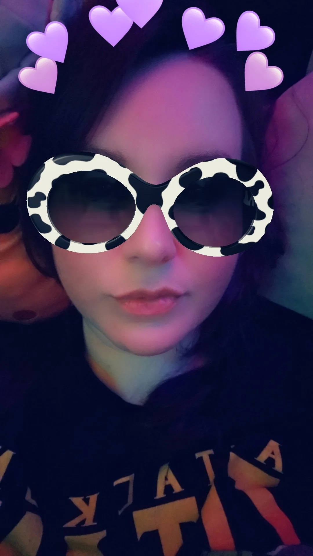 Selfie of a person wearing cow-print glasses with pink heart stickers and colorful lighting