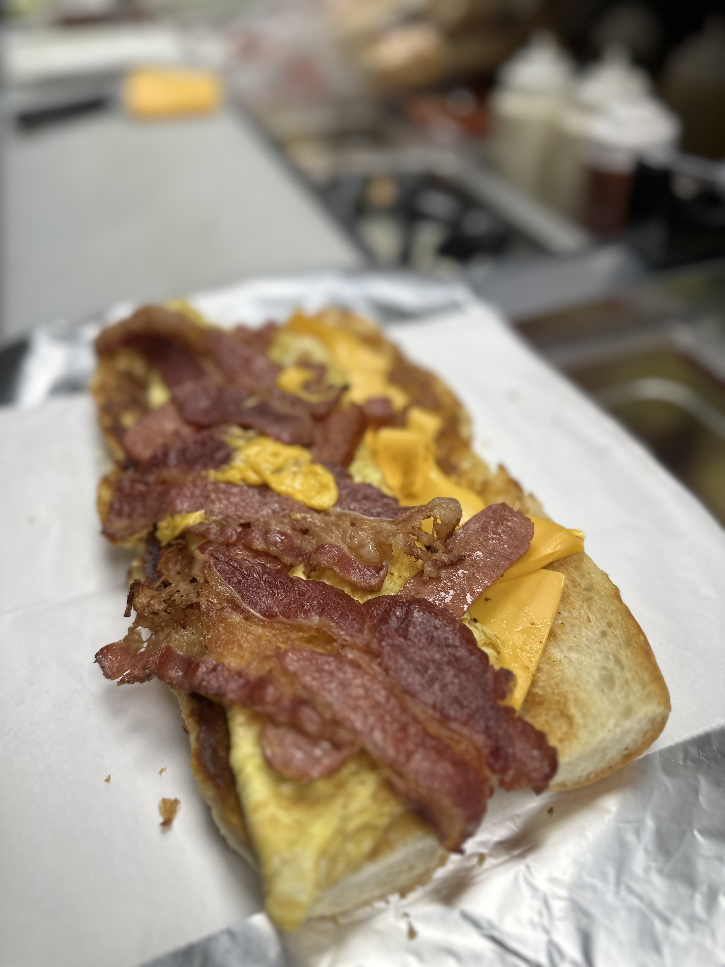 Close-up of a breakfast sandwich with bacon, egg, and cheese on a toasted bun, on a sheet of wax paper.