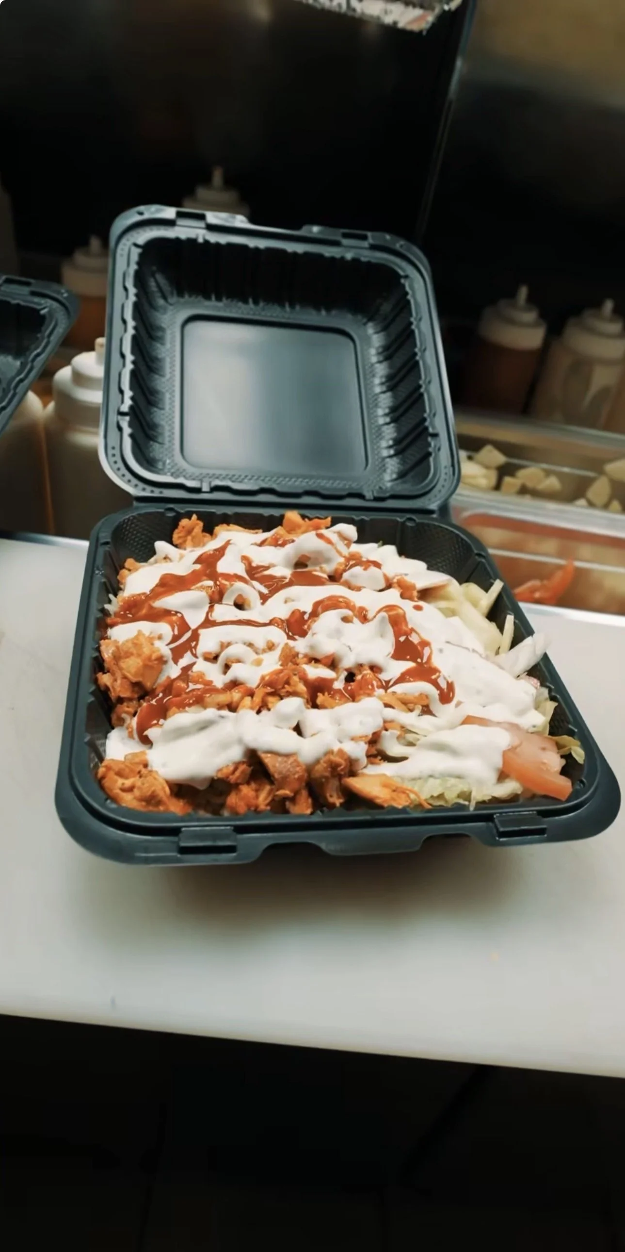 A black takeout container filled with shredded meat, lettuce, tomatoes, and condiments including sour cream and hot sauce.