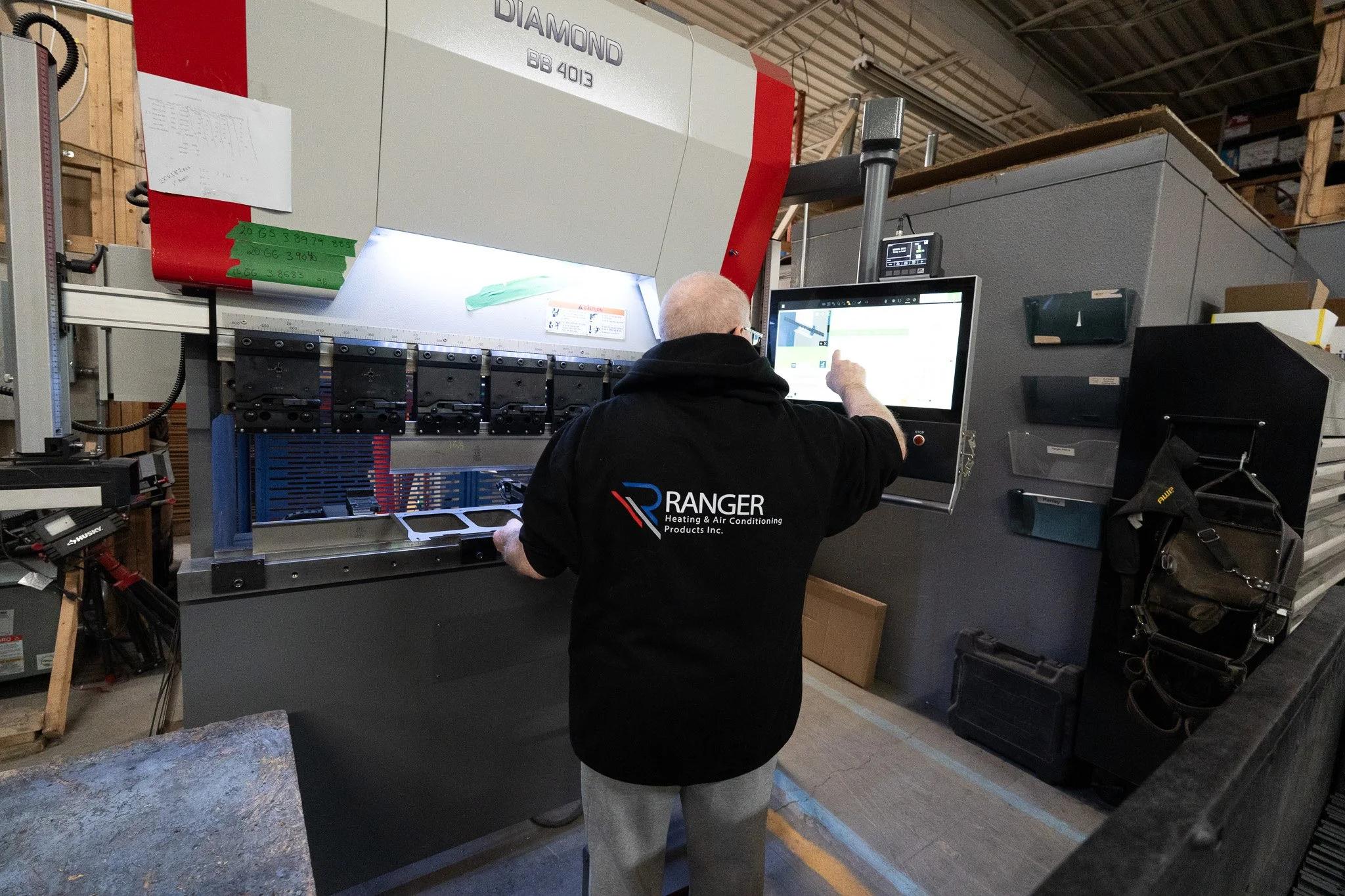 A worker operating a computer at a manufacturing machine in an industrial factory setting.