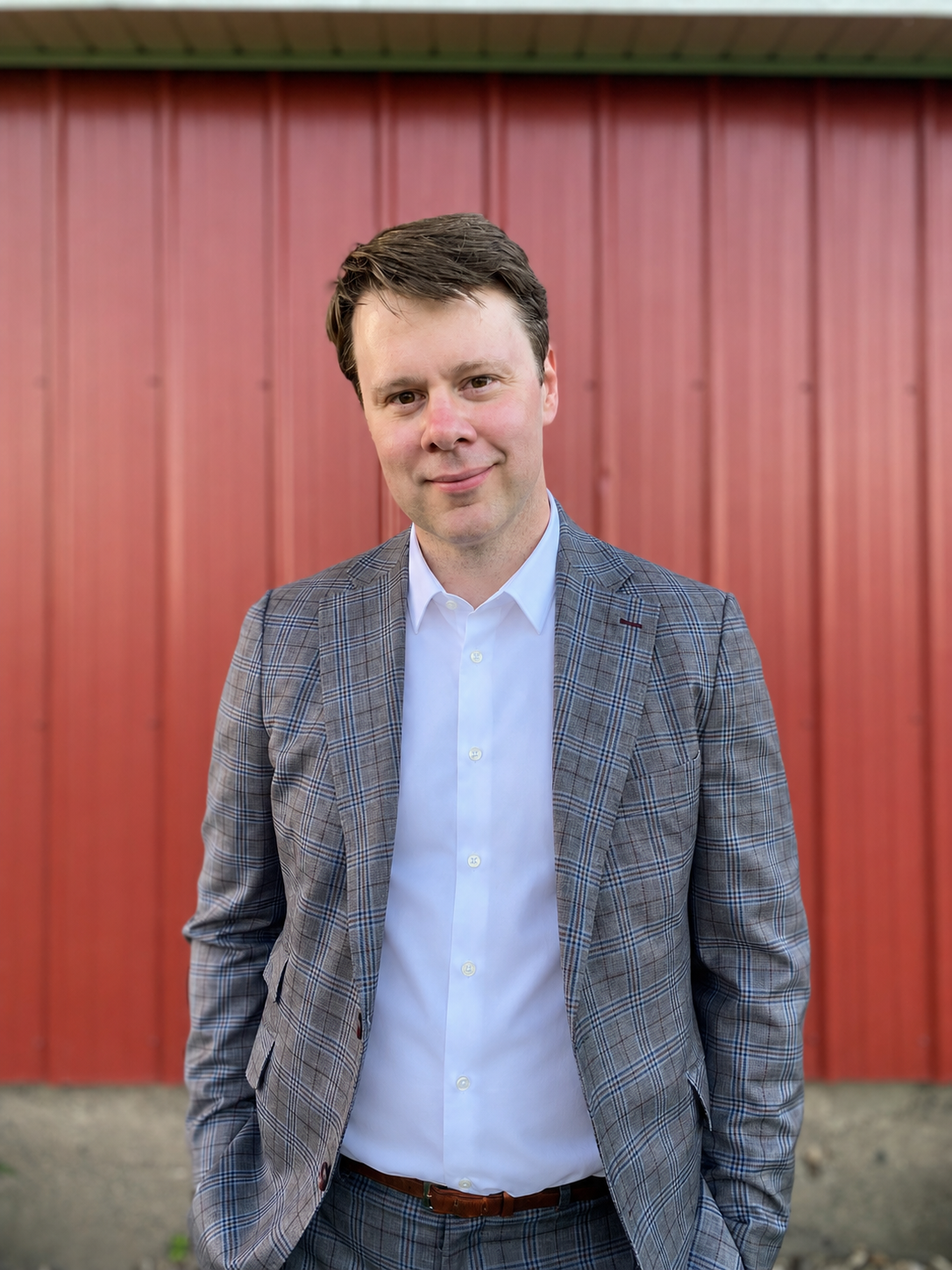 Steve Borchardt standing outdoors in a suit in front of a red barn.