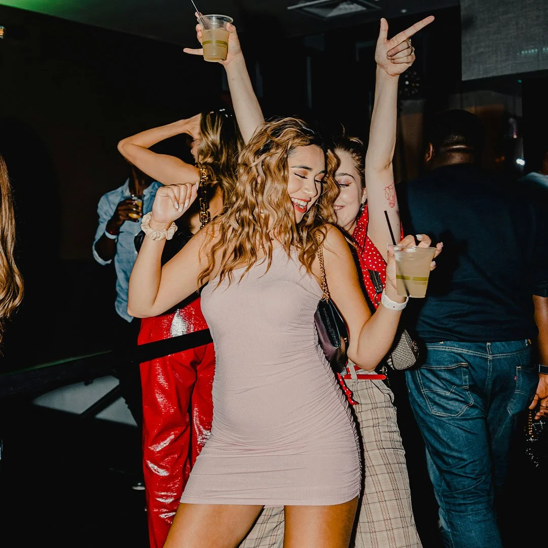 Group of people dancing and having fun at a party, holding drinks, in a lively environment.