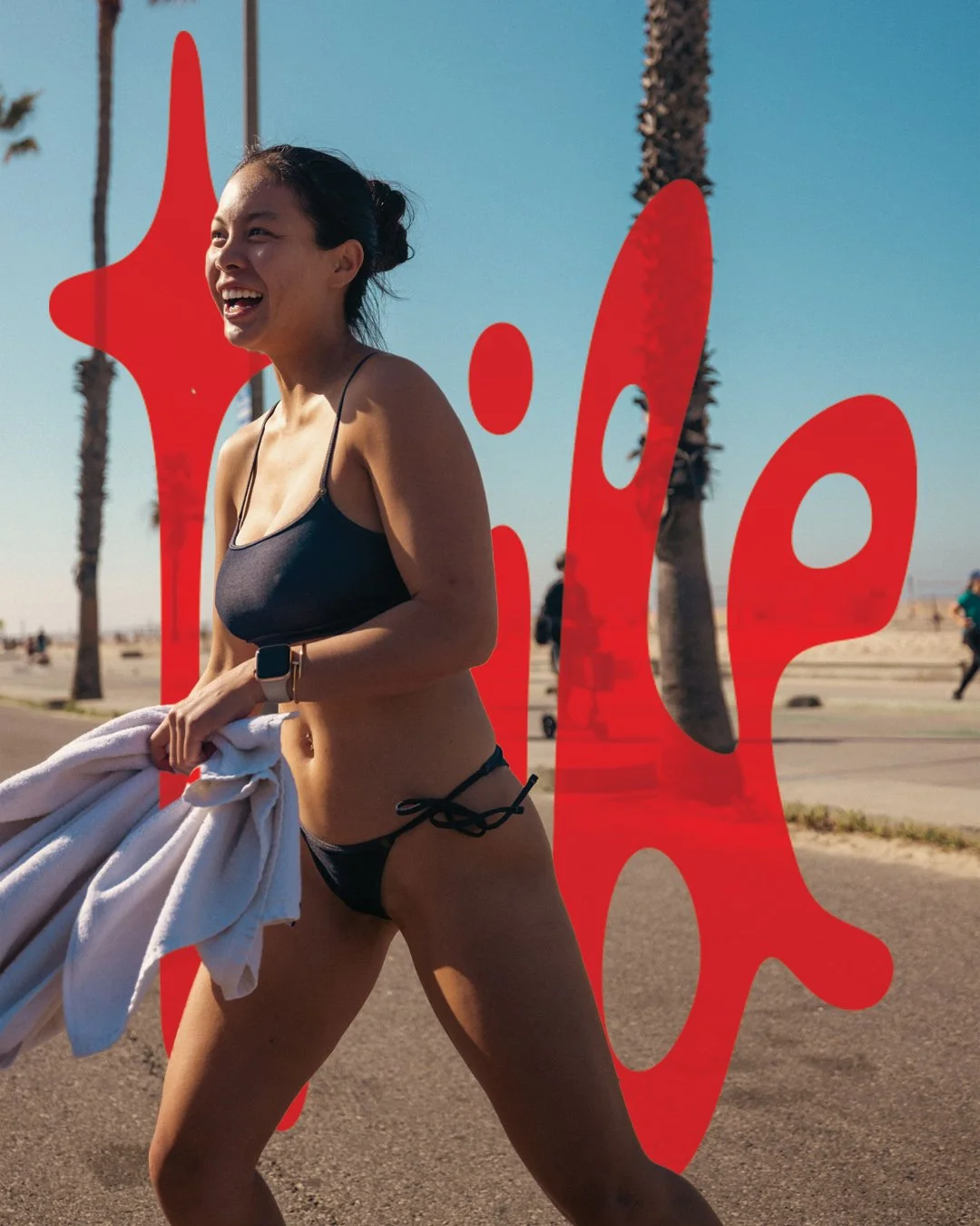 A woman in a black bikini smiling and holding a towel, jogging or walking outdoors near the beach with palm trees in the background, and a red paint splash overlay.
