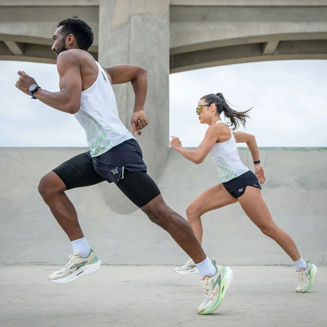 Two runners, a man and a woman, sprinting outdoors under a concrete bridge.