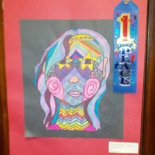 Colorful abstract drawing of a woman's face with rainbow-colored hair and geometric patterns, including a '1st Place' ribbon on the side.