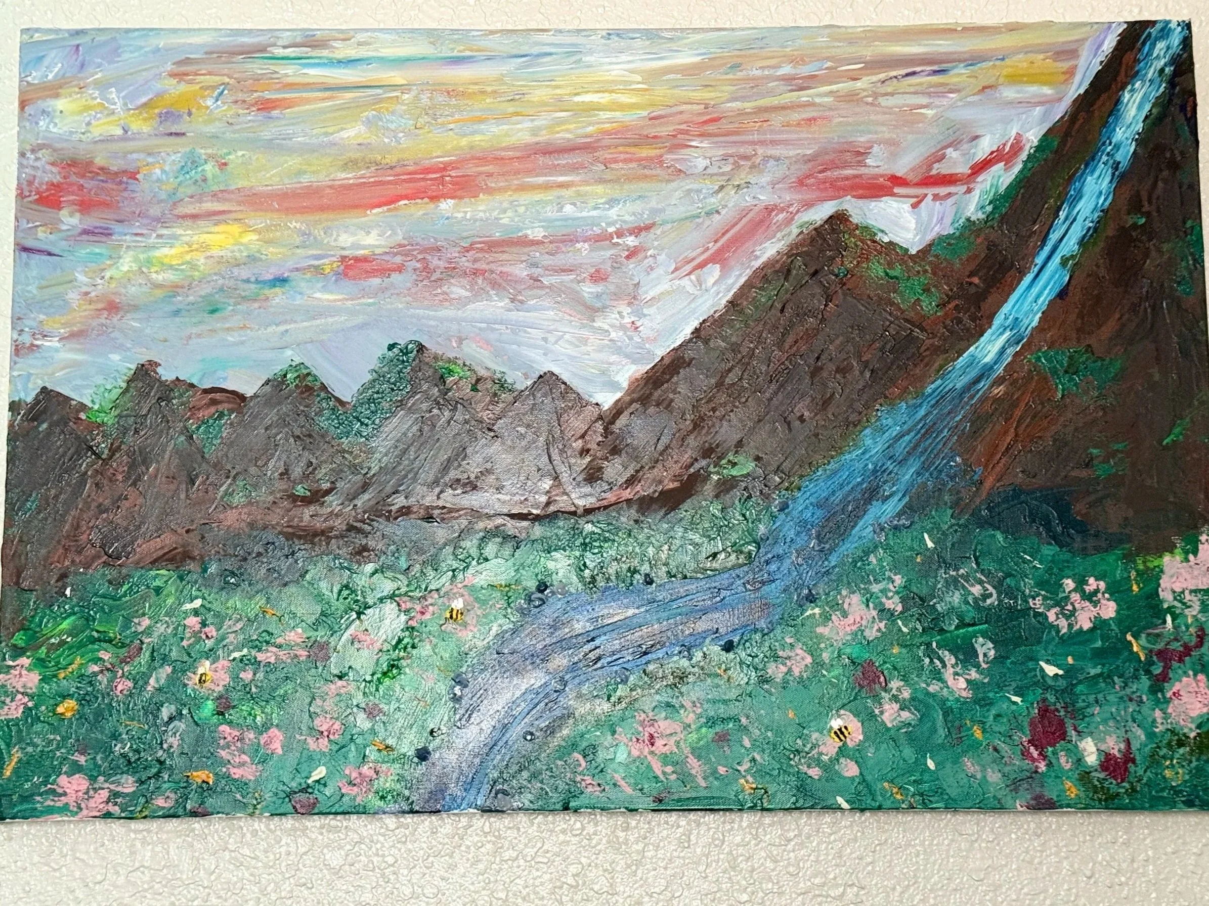 A painting of a mountain landscape with colorful sky, tall rugged mountains, a rushing river, and flowering green fields.