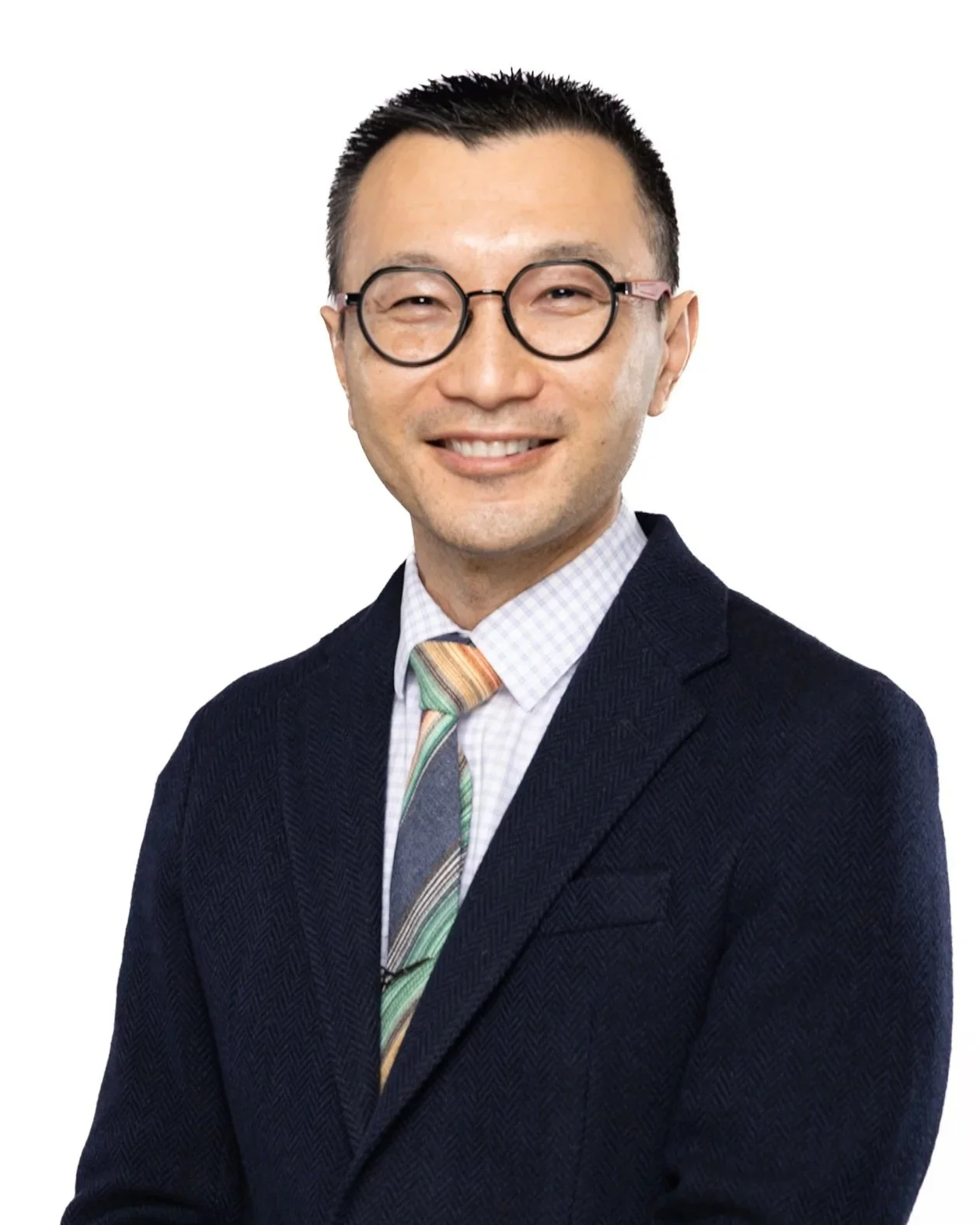 A smiling man wearing glasses, a dark blazer, a checked shirt, and a colorful striped tie, posing against a white background.