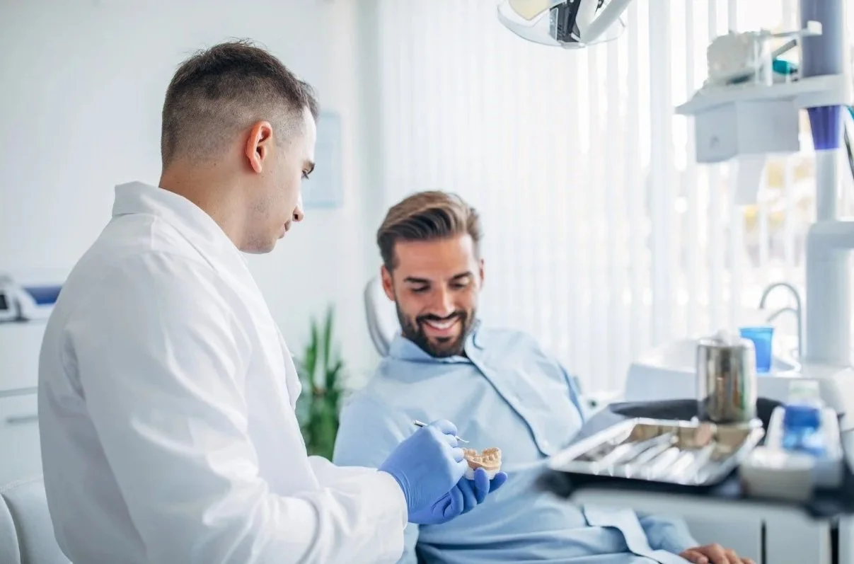 A dentist showing a dental prosthetic to a smiling male patient in a dental clinic.