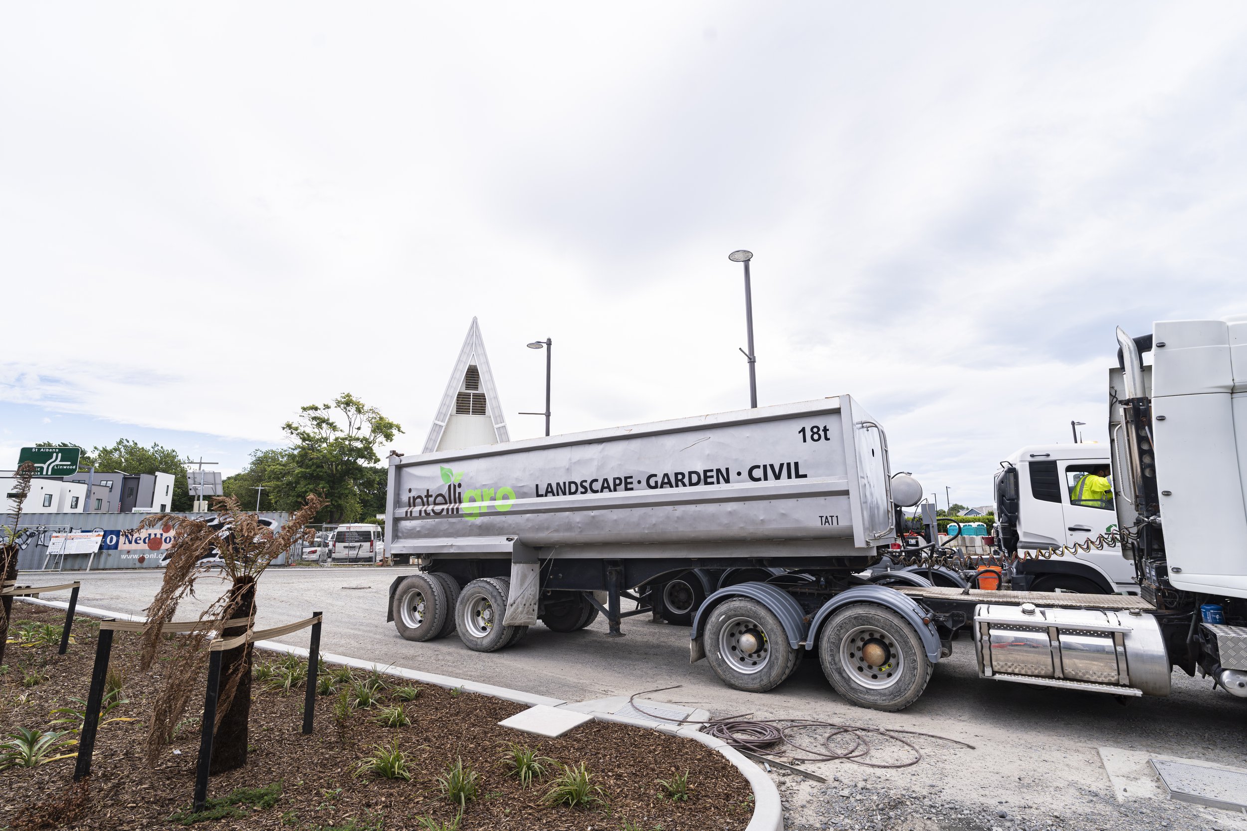 Construction truck parked at an outdoor site with trees, street signs, and a One stadium New Zealand in the background.