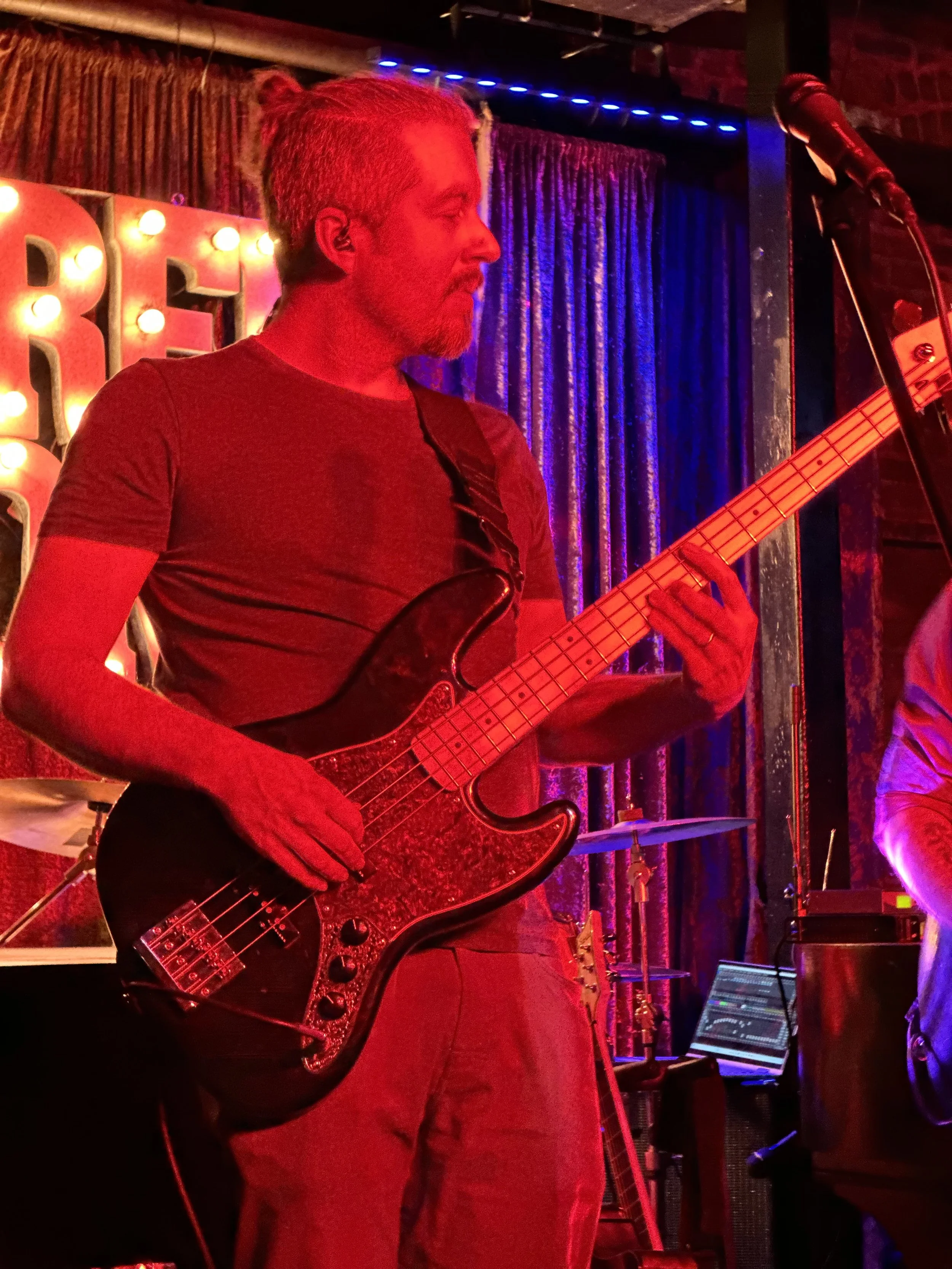 A male musician playing an electric guitar on stage, with colorful lighting and a microphone nearby.