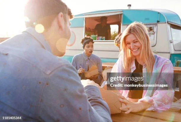 Group of friends at a food truck, smiling and enjoying outdoor conversation in the sunlight.