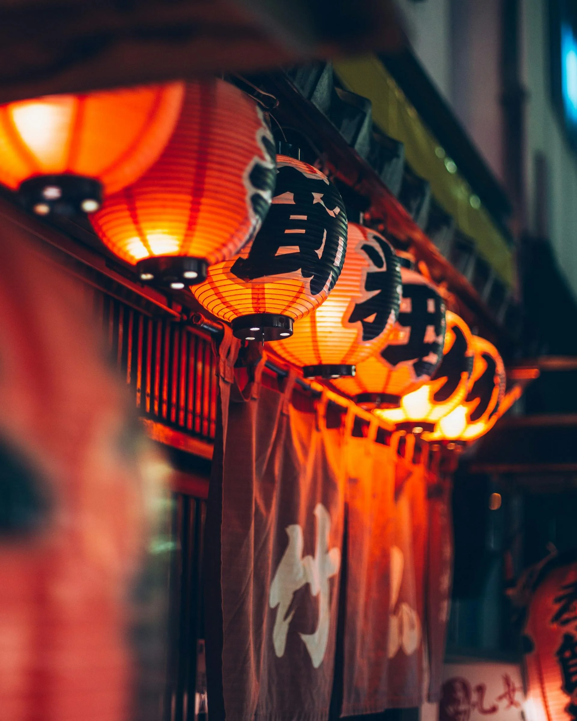 Red Japanese paper lanterns with black kanji characters hanging in a row at night.