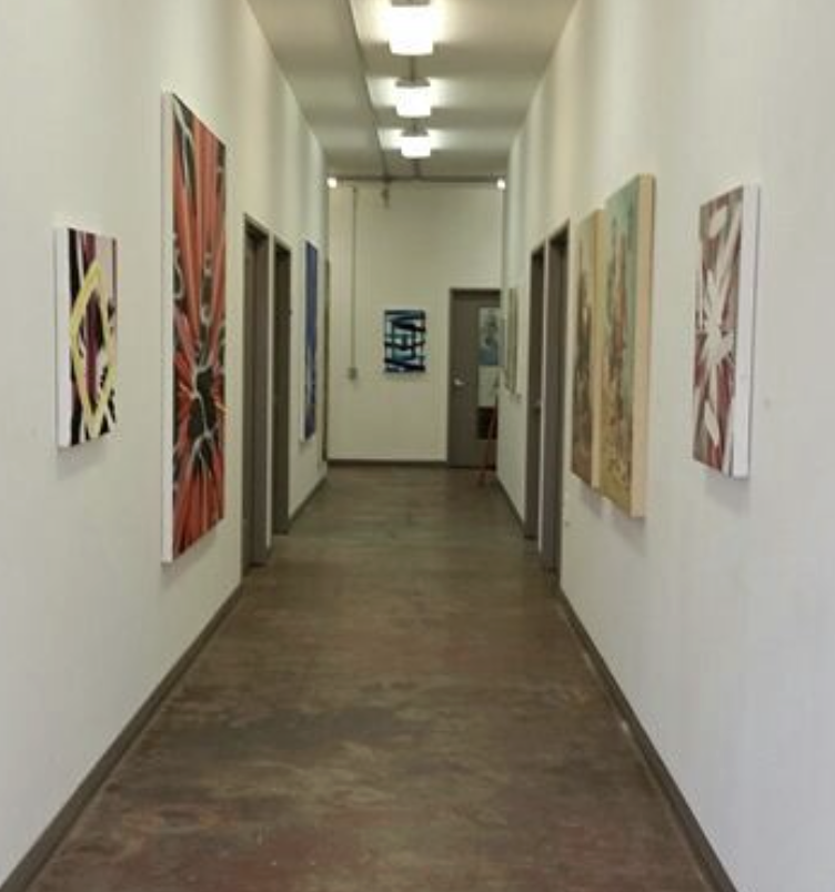 Art gallery hallway with colorful abstract paintings on white walls and wooden flooring.
